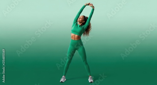 Athletic Woman Stretching Hands Up in Green Activewear on Gradient Green Studio