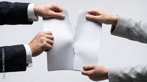 Hands of two business people tearing a blank paper document apart. Powerful concept for broken contracts, business conflict, partnership dissolution, divorce, and canceled agreements