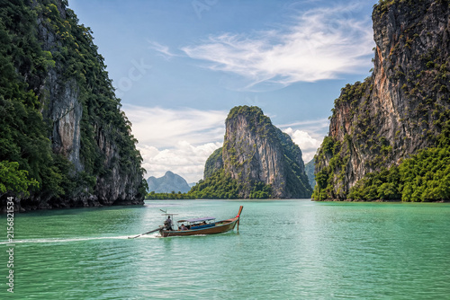Longtail boat floating in a calm green lagoon enclosed by steep limestone cliffs near Phuket.generative AI