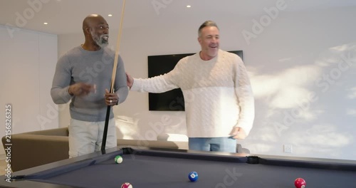 Diverse men at pool table watching senior man striking cue, scattering balls, playing, cheering