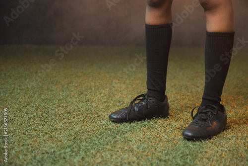 Woman standing on turf at studio wearing black knee-high socks and untied soccer shoes, copy space