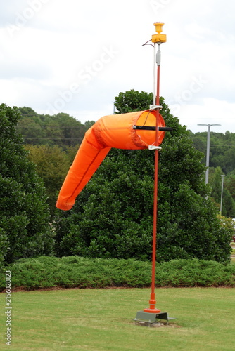 Foto Bright orange windsock mounted on a tall pole against trees and cloudy sky background
