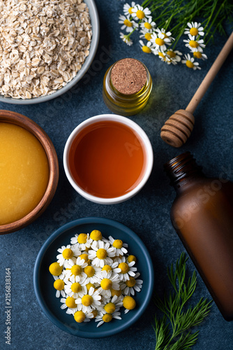 Photo, organic ingredient flat lay with oats, honey, chamomile flowers and amber glass bottles, warm natural daylight, no watermark., highlighting the exquisite textures and vivid environment