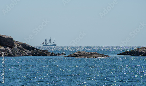 Foto Distant sailing ship framed by granite islets and blue water.