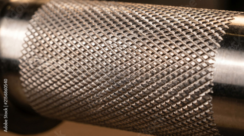 Textured steel surface of a workout barbell catching the bright light