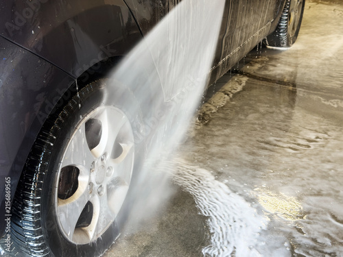 Washing a dark car wheel and lower body with a high-pressure water jet stream at a car wash.