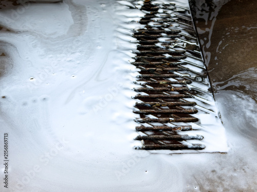 White soapy foam flowing into a metal drainage grate on a wet concrete floor at a car wash