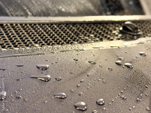 Close-up of water drops and beads on a dark car hood showing hydrophobic coating effect