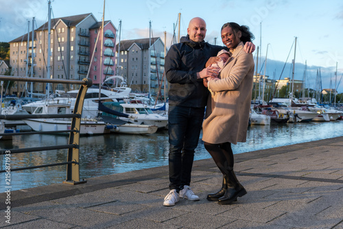 Happy Interracial Couple Holding Newborn Baby at Marina During Golden Hour