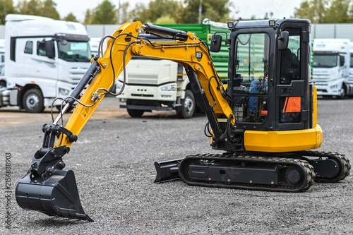 Mini excavator and other construction machinery parked in an equipment yard. Heavy equipment ready for work, transport, or use at construction and infrastructure sites.