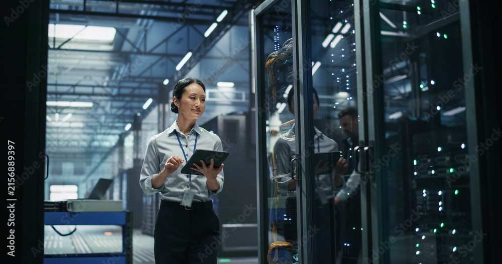 Fototapeta premium Asian Female Data Engineer Using Digital Tablet Computer Beside Server Cabinet, Performing Firmware Audit and Cable Management Review in High Performance Machine Learning Supercomputer Facility.
