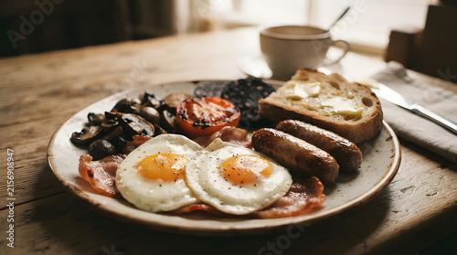 Classic full English breakfast plate with eggs, bacon, sausage, beans, toast, and black pudding on wooden table