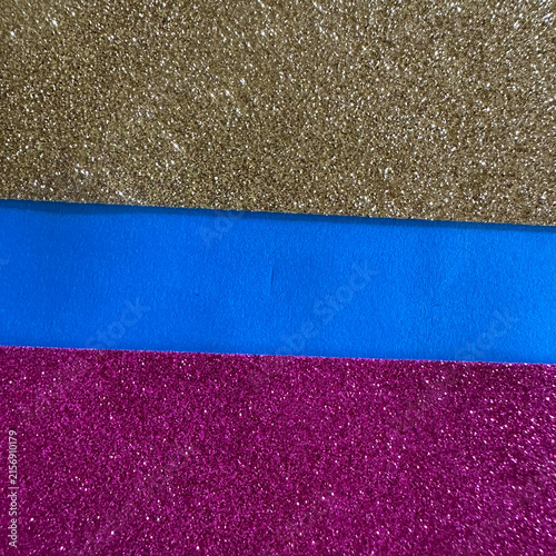 Horizontal bands of gold glitter, blue paper, and magenta glitter texture