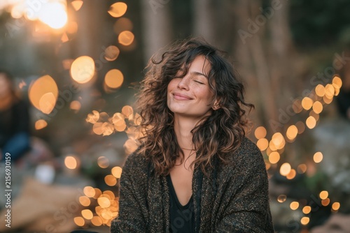 Mindfulness and well-being happy woman with closed eyes smiling in a relaxed outdoor setting with bokeh lights