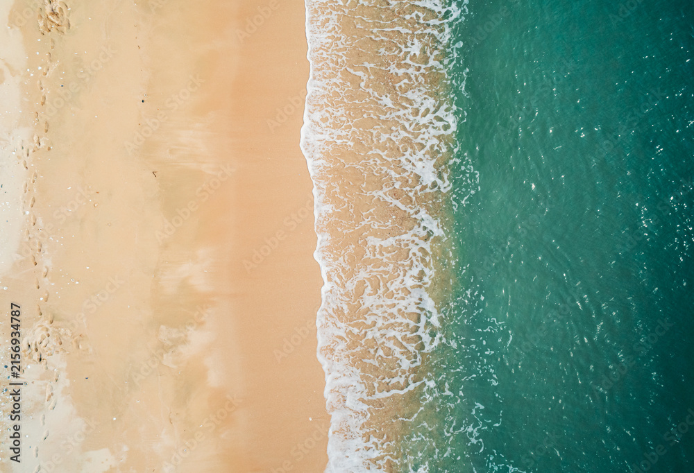 Fototapeta premium Aerial view of sandy beach and turquoise ocean. Top view of ocean waves reaching shore on sunny day.
