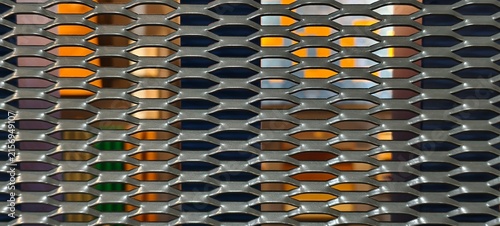Photography Shiny metallic mesh with elongated diamond pattern, foreground sharply focused against colorful blurred vertical lights in orange, blue, green, and purple