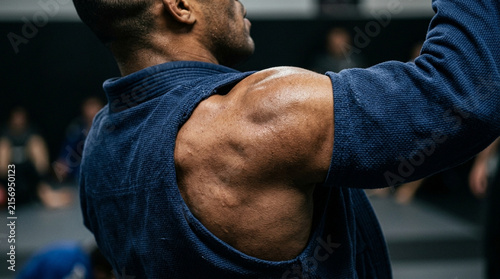Athlete's muscular shoulder in Jiu-Jitsu gi, close-up, focused training