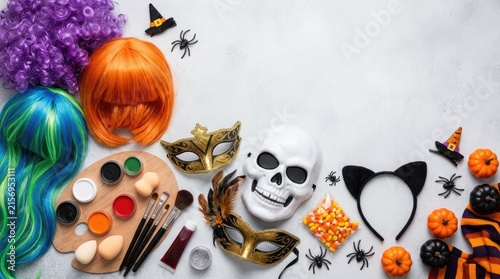 A festive Halloween flat lay arrangement showcases various costume and makeup items. A vibrant blue and green wig sits next to an orange wig and a miniature pumpkin.