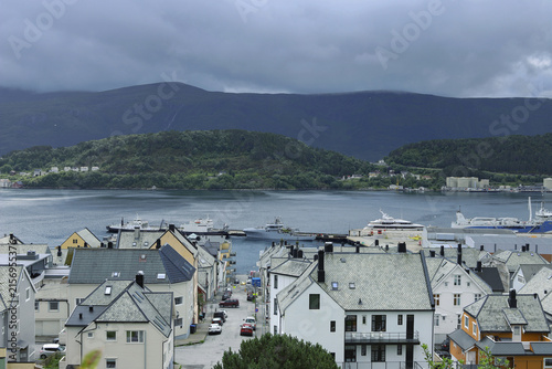 Traditional coastal houses and harbor in Alesund town, Norway. Scandinavian cityscape with ocean bay, mountains under dramatic sky.