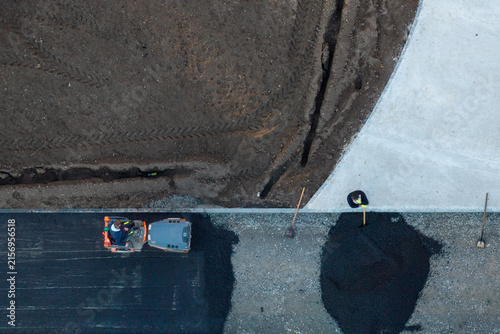 Belgrade, Serbia - 14 November 2025: Aerial view of workers laying new asphalt during road construction, with a steamroller compacting the surface and a worker using a shovel near a pile of gravel.