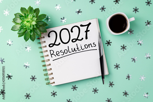 New year resolutions 2027 on desk. 2027 goals list with notebook, coffee cup, plant on blue table. Resolutions, plan, goals, action, checklist, idea concept. New Year 2027 resolutions, copy space