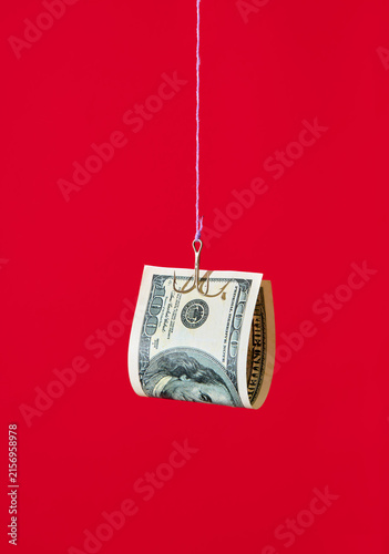 One hundred dollar bill on fishing hook over red background