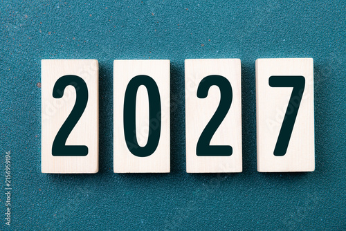 2027 Happy New Year. Wooden cube block 2027 greeting card on green. Concept 2027 New Year background. Business, resolutions, goals, inspiration, success, ideas
