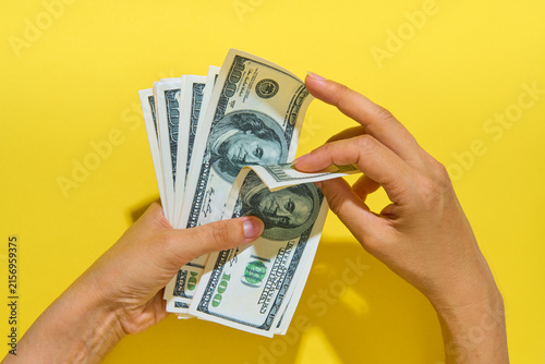 Hands counting hundred dollar bills on yellow background
