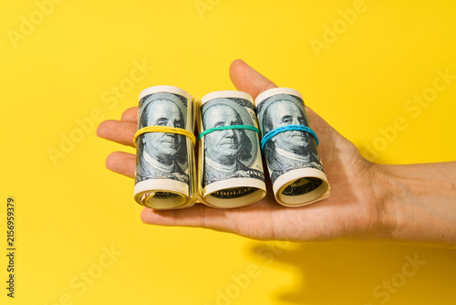 Hand holding three rolls of hundred dollar bills