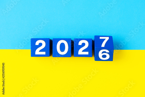 2027 Happy new year. Flipping of wooden cube block change from 2026 to 2027 on yellow and blue background ukrainian flag. Politics, support for Ukraine, resolutions, goals, business, success ideas