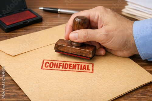 A stamper with the word 'confidential' on it sits on top of a piece of paper, ready for use