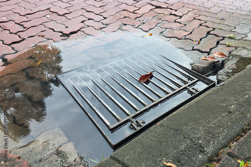 Fotografie Puddle of water on clogged drain outlet with leaf on street risk flooding during