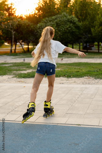 Canvastavla A lovely fair-haired girl is skating on yellow roller skates in the golden hour
