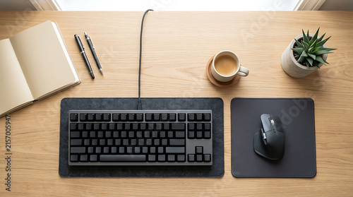 Modern wooden office desk setup with keyboard, mouse, notebook, coffee cup, and plant viewed from above