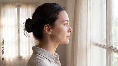 Contemplative young woman with hair bun looking out window with thoughtful woman profile profile gazing natural light