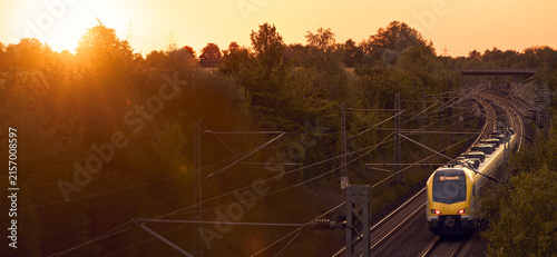 Intercity train traveling through a scenic railway corridor at sunset, surrounded by trees and overhead power lines. Stuttgart to Mannheim, Baden-Württemberg, Germany
