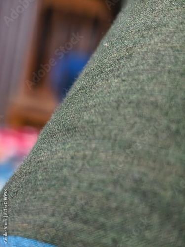 Close up of dark green textured fabric with a slight sheen and blurred background of wood and color