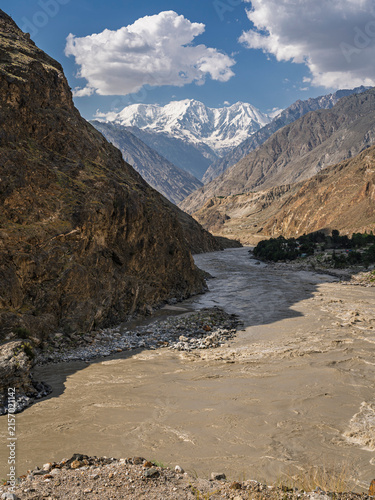 Scenic vertical landscape view of muddy river in mineral valley with mighty snowcapped Haramosh peak in background, Gilgit Baltistan, Pakistan