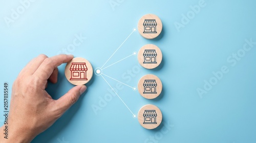 Hand holding wooden block representing business expansion strategy connecting multiple retail store locations