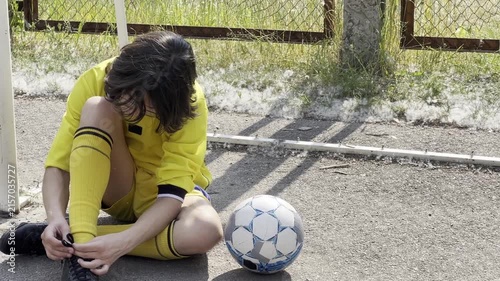 Teen soccer player sitting on court adjusting boots and laces during training session rest moment equipment and preparation youth sport concept. High quality FullHD footage