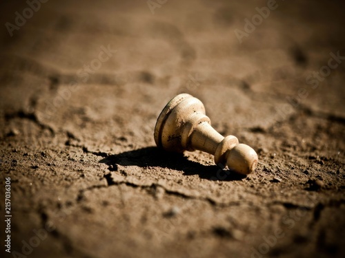Fallen White Chess Pawn on Cracked Dry Ground Symbolizing Defeat or Despair