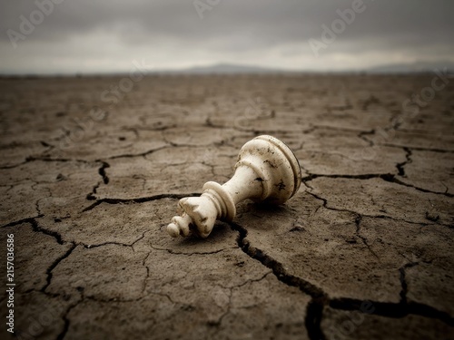 Fallen white chess piece on dry cracked desert ground under gloomy sky