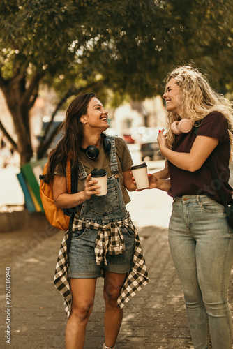 Quadro su tela Two young women friends laughing enjoying coffee outdoors