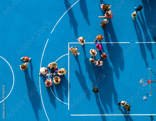 Belgrade, Serbia - 01 December 2025: Aerial view of children gathering and playing during a school recess on a blue outdoor basketball court.