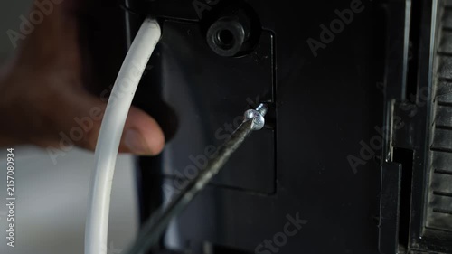 Close-up of a screwdriver removing a screw from a black appliance beside a white tube