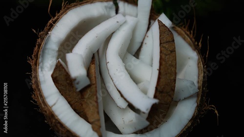 Sliced coconut pieces inside a half coconut shell on a dark background, showing fresh white flesh and brown husk