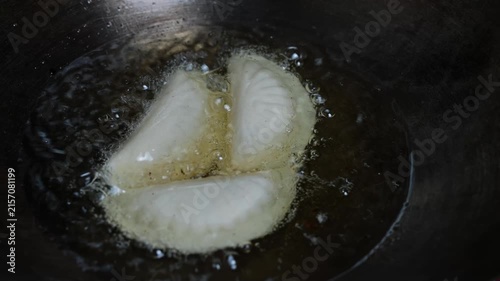Dumplings frying in hot oil in a dark pan, with bubbles around the dough pieces during cooking