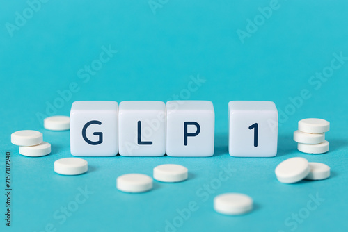 GLP 1 word on blocks surrounded by medicine pills on blue background. Copy space