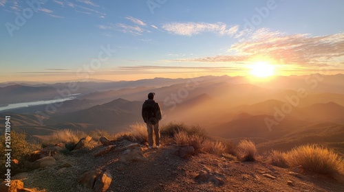 Hiker standing on rocky mountain peak watching sunrise with solitary figure