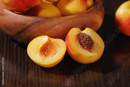 Ripe nectarines in a wooden bowl with a halved fruit showing its pit